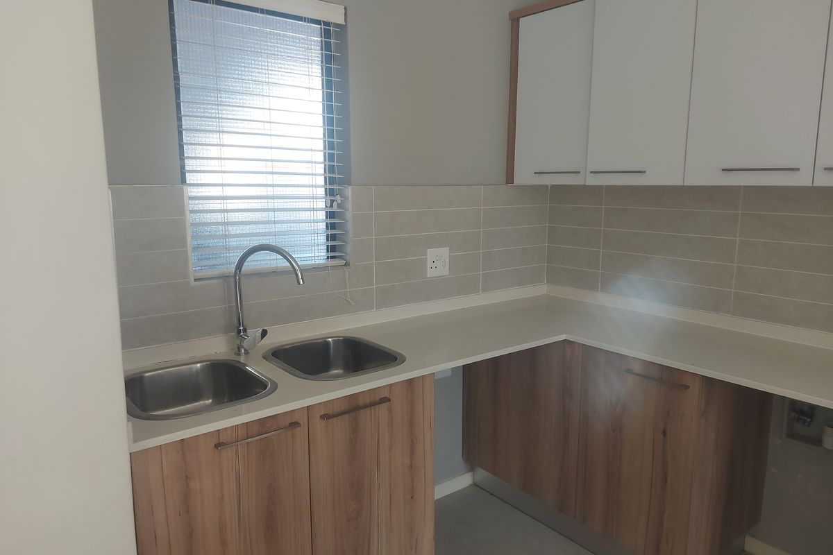 A clean, modern kitchen featuring double stainless steel sinks, wood-finish cabinetry, and neutral tiled splashbacks, offering a functional and well-maintained workspace.