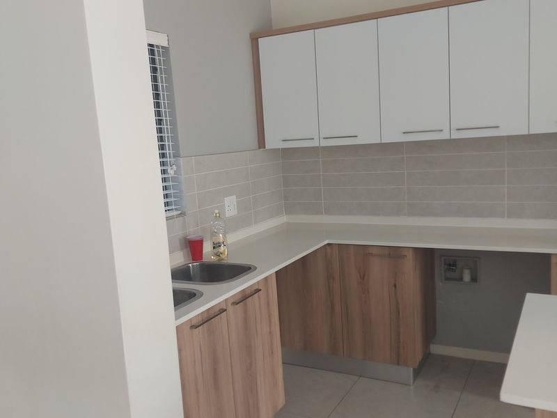 A clean, modern kitchen featuring wood-grain lower cabinets, white upper cabinets, tiled backsplash, and tiled flooring with dedicated appliance plumbing.