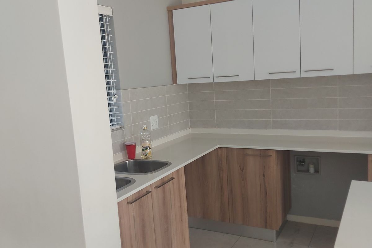 A clean, modern kitchen featuring wood-grain lower cabinets, white upper cabinets, tiled backsplash, and tiled flooring with dedicated appliance plumbing.