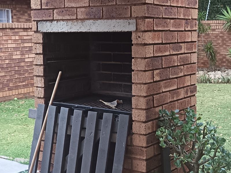 A backyard area featuring a traditional built-in brick braai and a well-maintained lawn enclosed by a brick boundary wall.