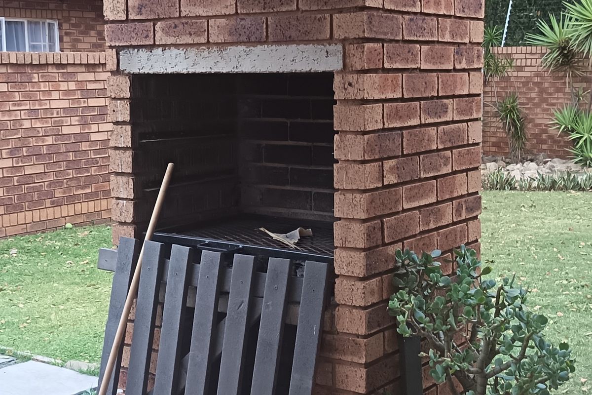 A backyard area featuring a traditional built-in brick braai and a well-maintained lawn enclosed by a brick boundary wall.