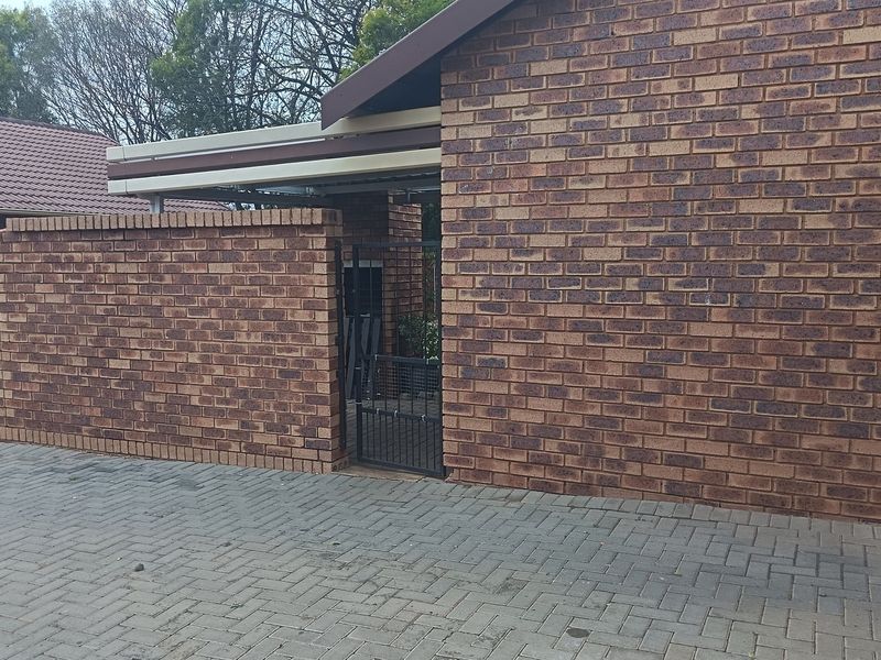 A view of the property's front exterior featuring a face brick boundary wall, paved driveway, and a secure metal pedestrian gate leading to the entrance.