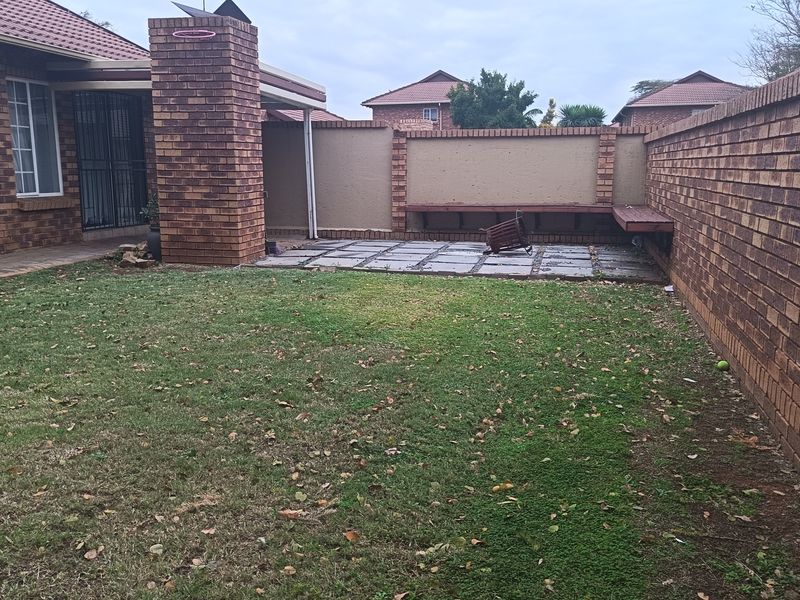 Rear garden featuring a paved patio area, built-in brick fireplace, and perimeter brick boundary walls with integrated wooden bench seating.