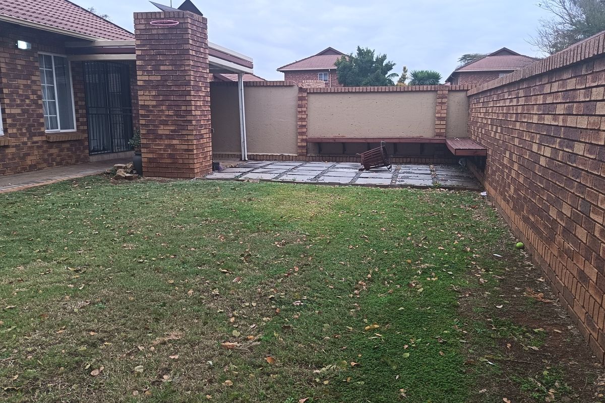 Rear garden featuring a paved patio area, built-in brick fireplace, and perimeter brick boundary walls with integrated wooden bench seating.