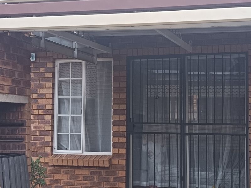 A covered patio area featuring a built-in brick braai, security gate, and exposed brickwork, providing a functional outdoor entertainment space.