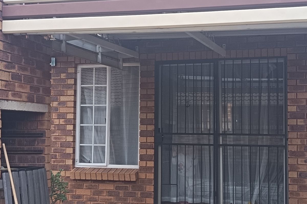 A covered patio area featuring a built-in brick braai, security gate, and exposed brickwork, providing a functional outdoor entertainment space.