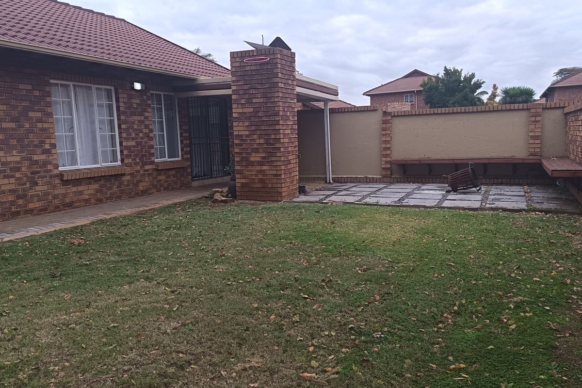 Rear exterior view featuring a face brick house, paved patio area with built-in fireplace, and a private garden with perimeter boundary walls.
