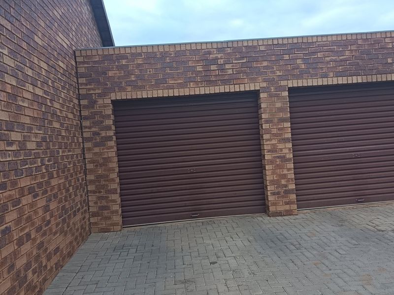A double garage featuring brown roller doors and a face brick exterior with a paved driveway.
