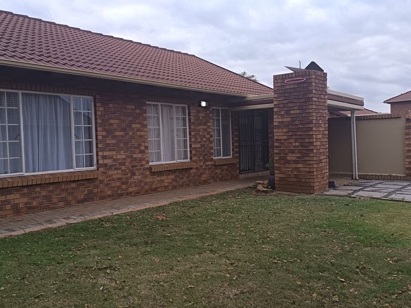 Rear view of a brick-faced house featuring a tiled roof, a brick chimney, and a paved walkway leading to a small garden area.