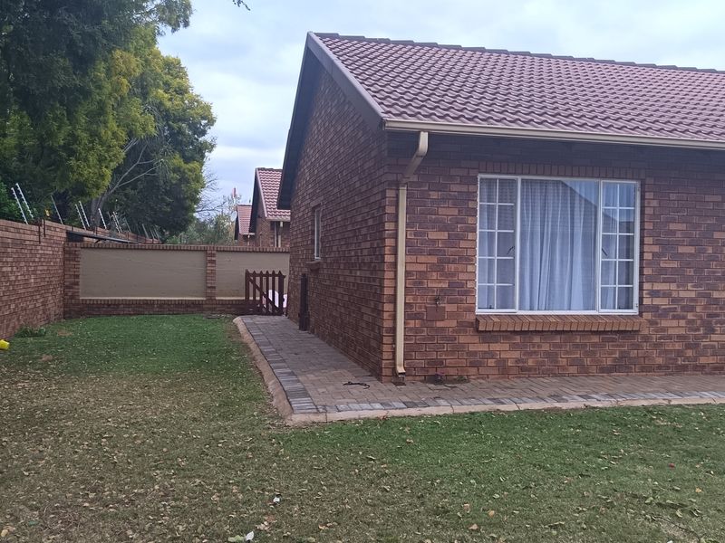 A view of the rear exterior of a face brick house featuring a paved walkway, lawn, and secure perimeter wall with electric fencing.