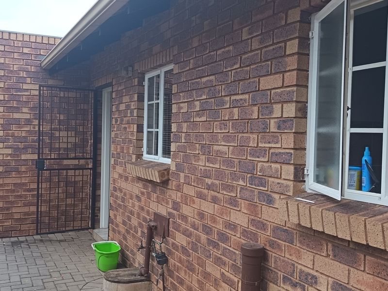A view of the rear exterior facade featuring face brick construction, paved patio area, security gate, and casement windows.