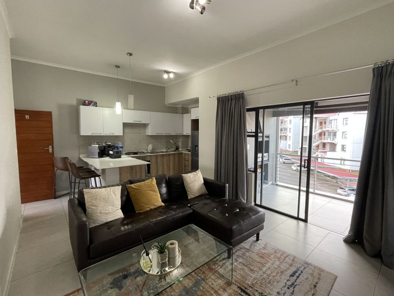Open-plan living area featuring a modern kitchen with built-in cabinetry, gas hob, and seamless access to a private balcony through sliding glass doors.