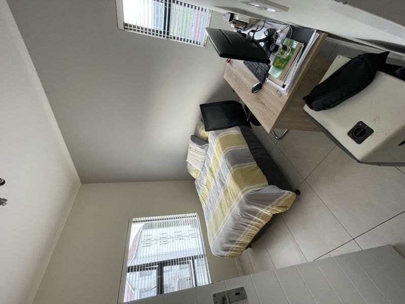 A well-lit bedroom featuring neutral tiled flooring, large windows with venetian blinds, and a clean, modern aesthetic.