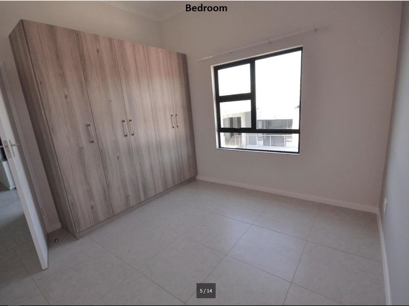 A bright, empty bedroom featuring modern tiled flooring and ample built-in cupboard storage with a neutral finish.