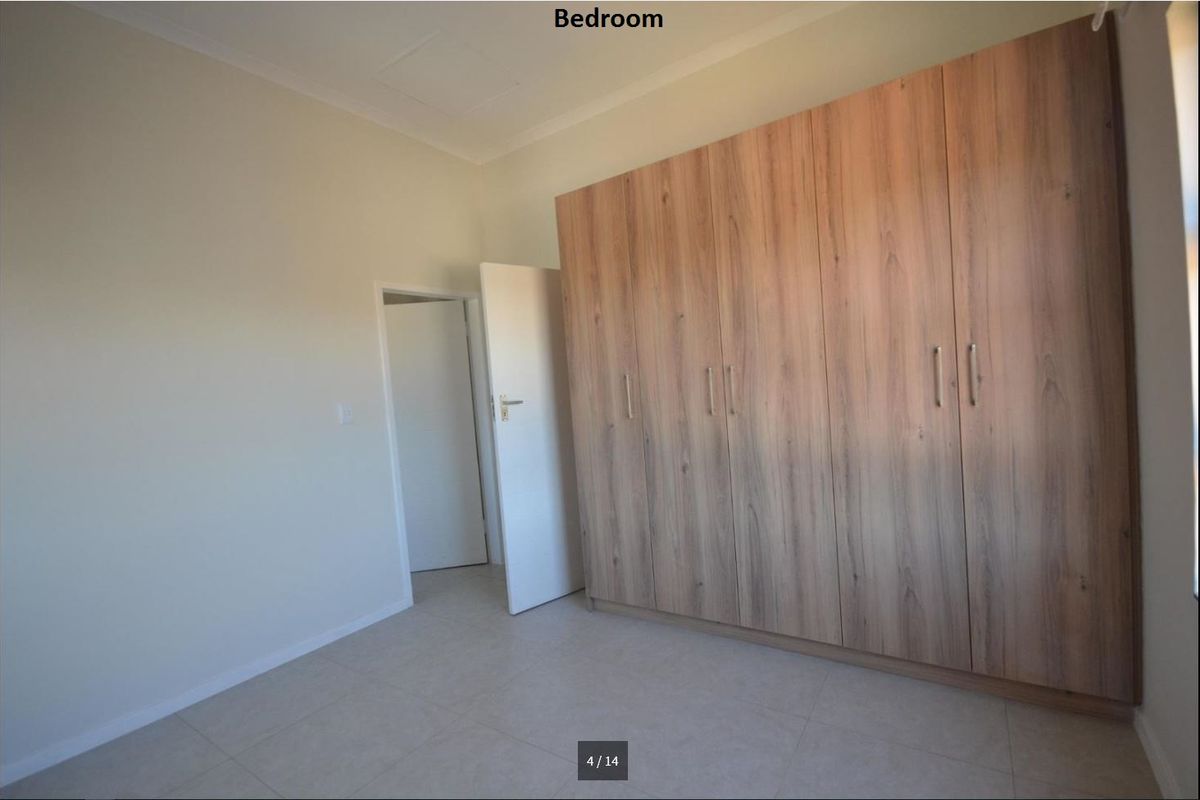 A clean, empty bedroom featuring neutral tiled flooring and extensive built-in wooden cupboards providing ample storage space.