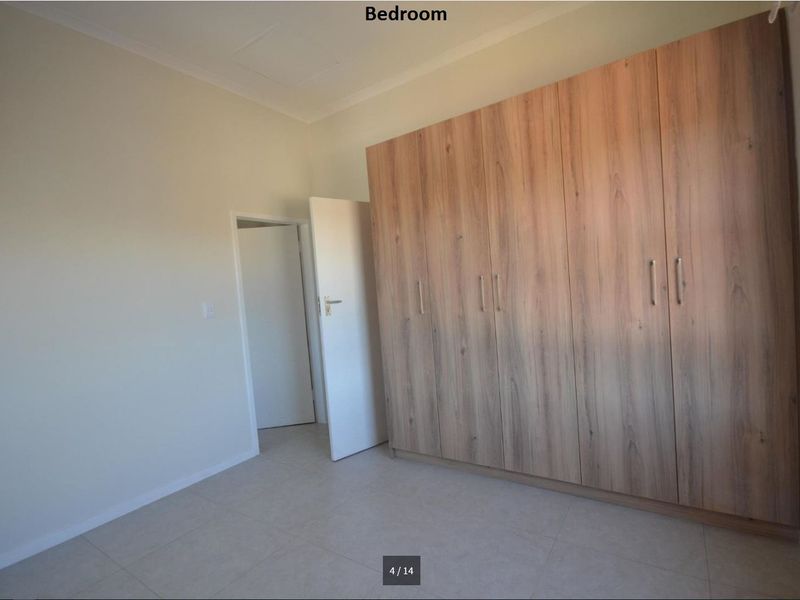 A clean, empty bedroom featuring neutral tiled flooring and extensive built-in wooden cupboards providing ample storage space.
