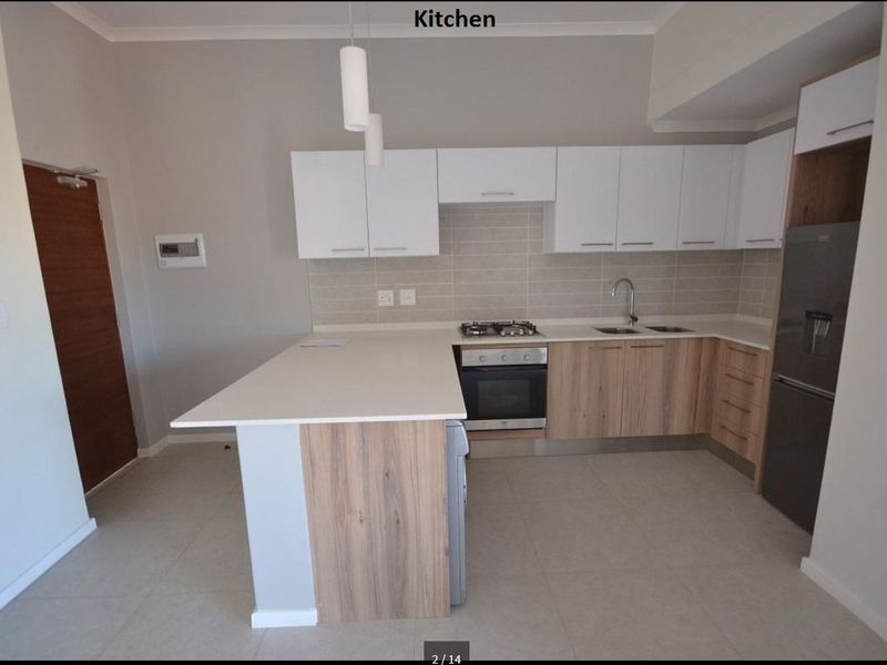 Modern kitchen featuring light wood-tone lower cabinets, white upper cabinetry, stone countertops, built-in oven, gas hob, and a functional breakfast bar peninsula.