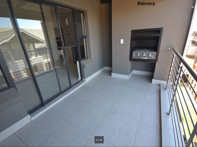A modern, covered balcony featuring tiled flooring, a built-in braai, and a metal balustrade, accessible via large sliding glass doors.