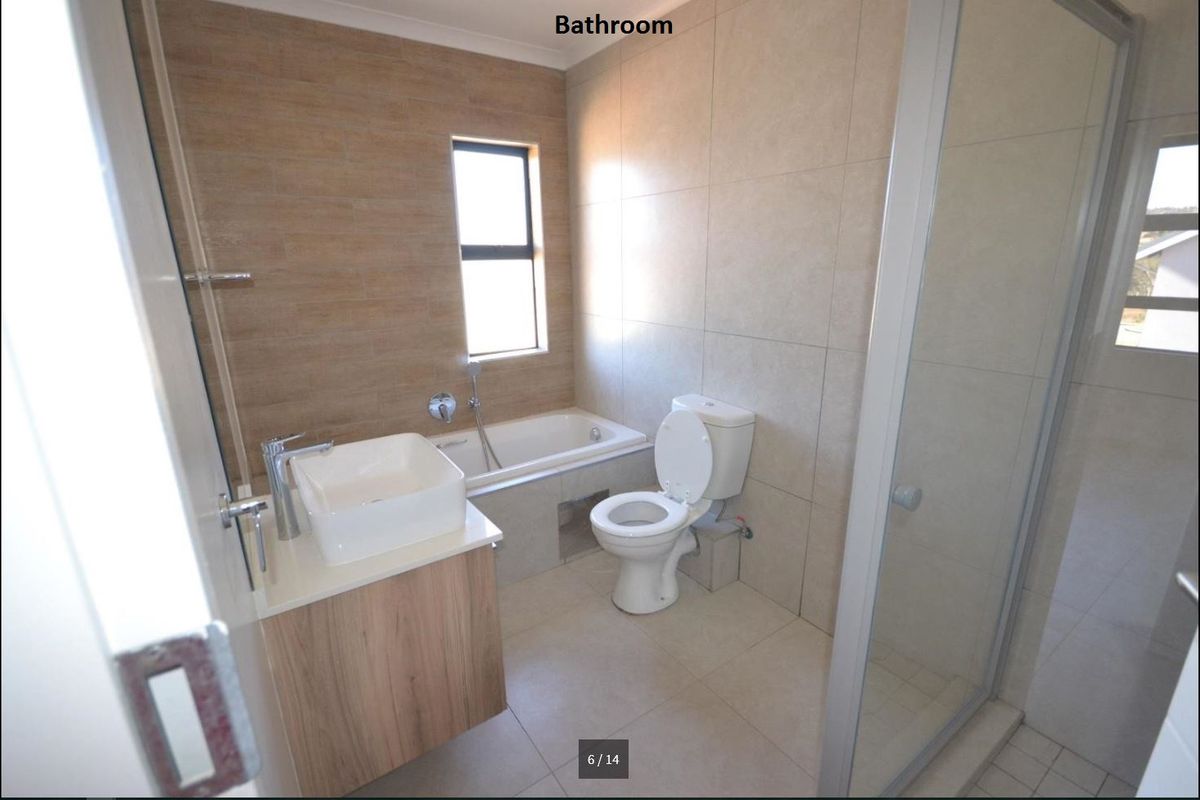 A modern bathroom featuring a built-in vanity with a vessel sink, a bathtub, a toilet, and a separate glass-enclosed shower with neutral tiling.