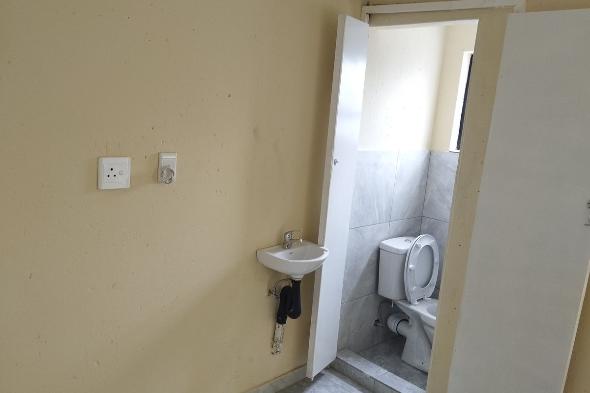 A small bathroom area featuring a wall-mounted basin and a separate toilet cubicle with tiled flooring and walls.