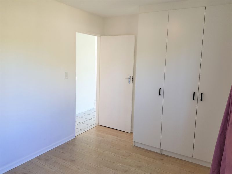 A clean, empty bedroom featuring light-toned laminate flooring and white built-in cupboards, offering a neutral space ready for personalization.