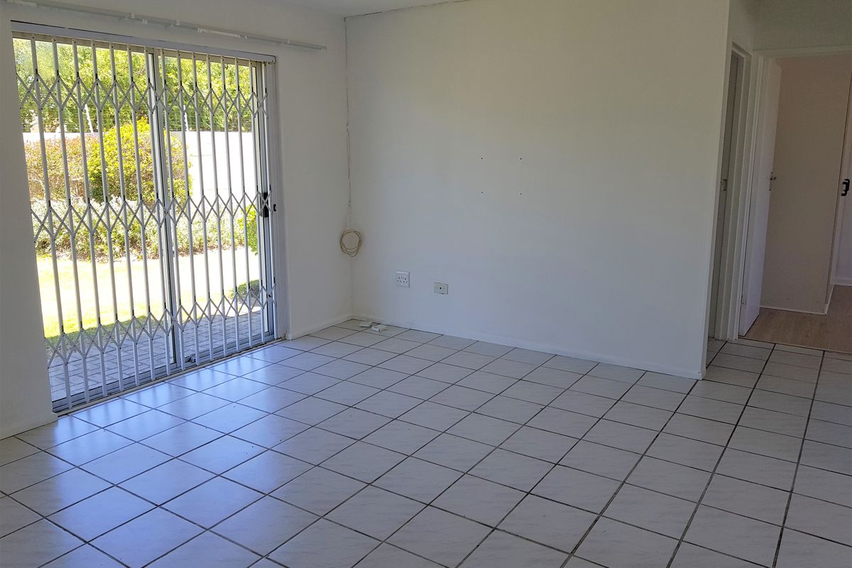 An empty living room featuring ceramic floor tiles and a sliding glass door with a security gate, providing direct access to the outdoor area.