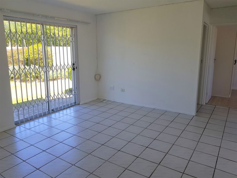 An empty living room featuring ceramic floor tiles and a sliding glass door with a security gate, providing direct access to the outdoor area.