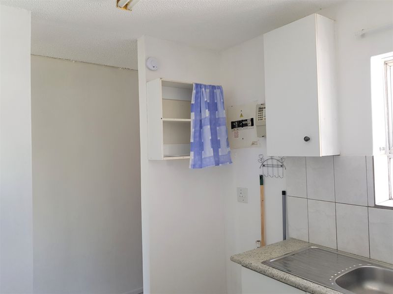 A compact kitchen area featuring a stainless steel sink, tiled backsplash, and wall-mounted cabinetry, currently in need of cosmetic updates and repairs.