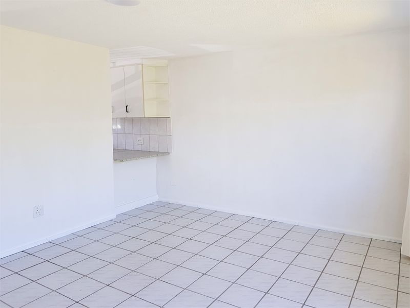 An empty open-plan living area featuring tiled flooring and a compact kitchen corner with built-in cabinetry and a tiled backsplash.
