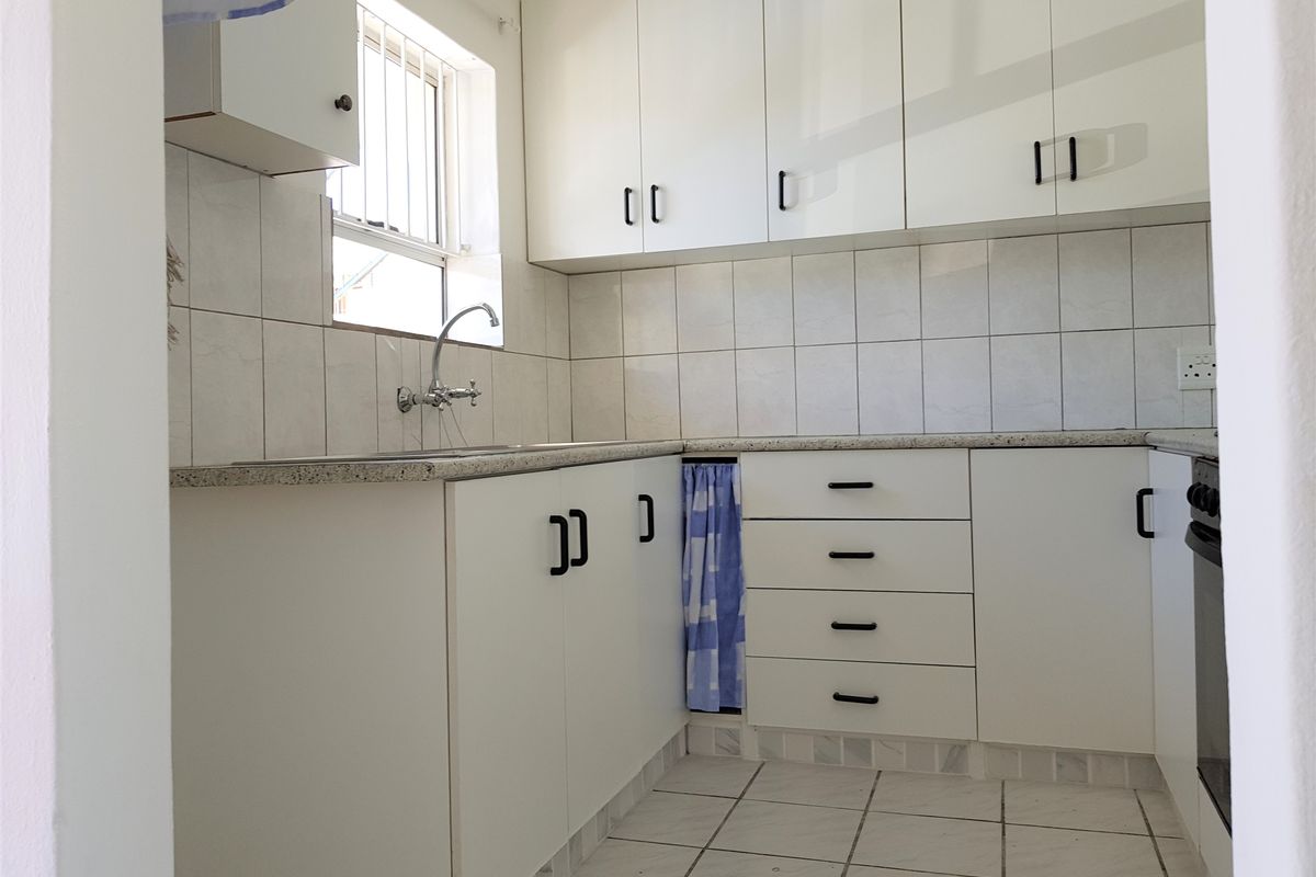 A functional kitchen featuring white built-in cabinetry, tiled backsplash, laminate countertops, and a built-in oven, offering a clean and practical workspace.