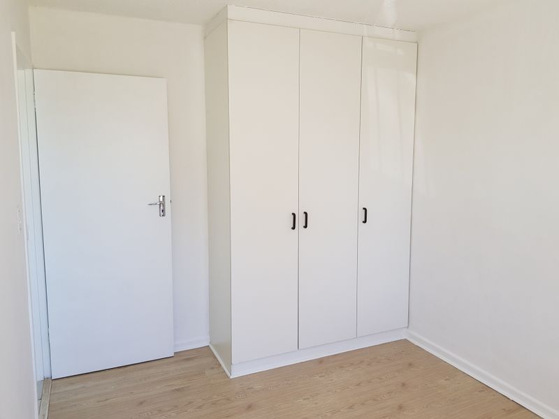 A clean, empty bedroom featuring light-toned laminate flooring and a modern white built-in wardrobe with black hardware.