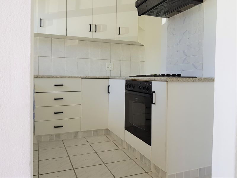 A clean, modern kitchen featuring white cabinetry, stone countertops, a built-in oven, gas hob, and extractor fan with neutral tiled finishes.