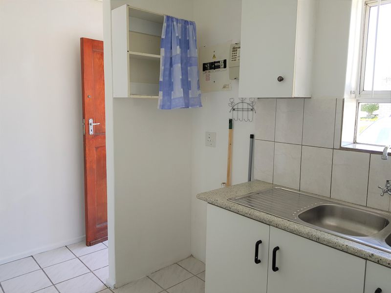 A compact kitchen area featuring built-in cabinetry, a stainless steel sink, tiled backsplash, and tiled flooring, presenting a functional but dated space.