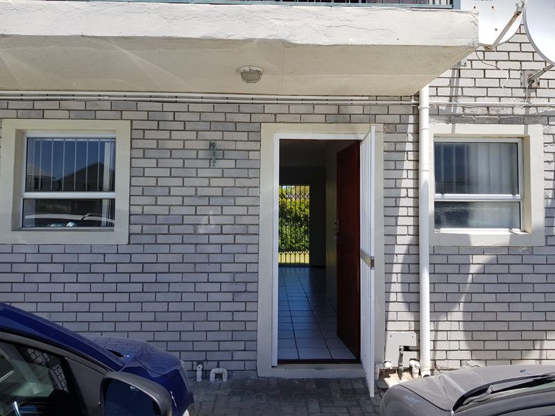 Front entrance of the apartment featuring a brick facade, security gate, and tiled interior flooring visible through the open doorway.