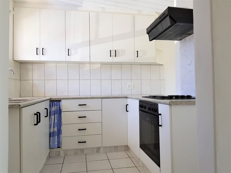 A functional kitchen featuring white cabinetry, a built-in oven with gas hob, extractor fan, and tiled finishes throughout.