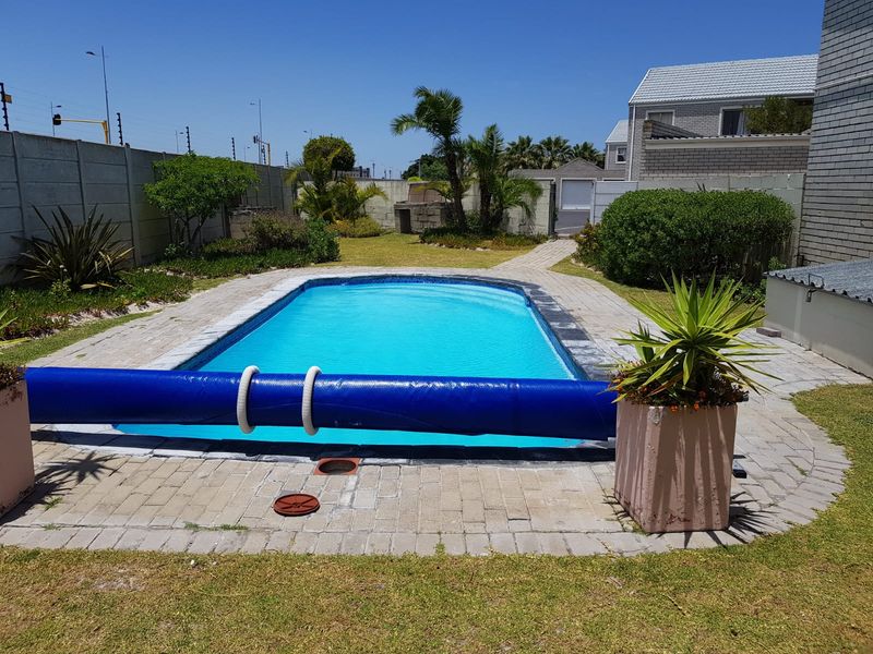 A well-maintained outdoor pool area featuring a paved surround, a pool cover, and a secure perimeter wall in a private garden setting.