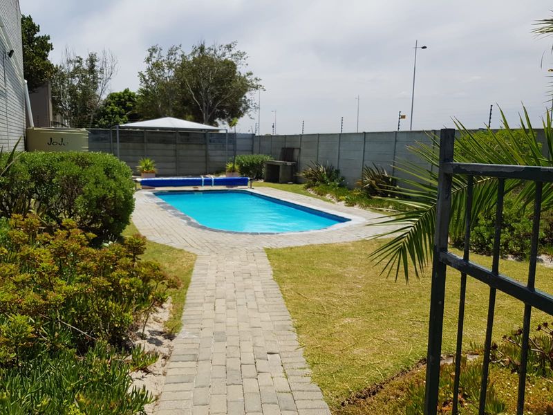 Outdoor pool area featuring a swimming pool with paved surround, brick pathway, built-in braai, and a secure precast concrete boundary wall.
