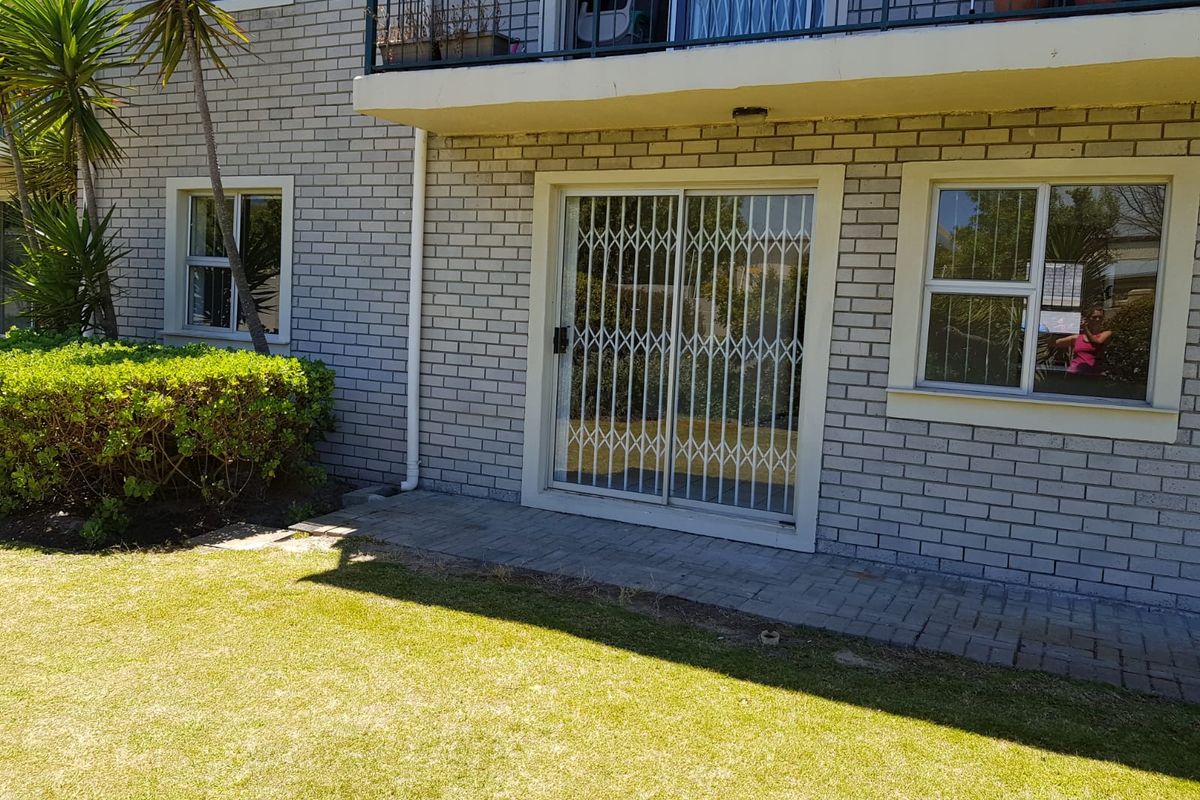 Rear exterior view of the apartment featuring a brick facade, a paved patio area, and a sliding door with a security gate.