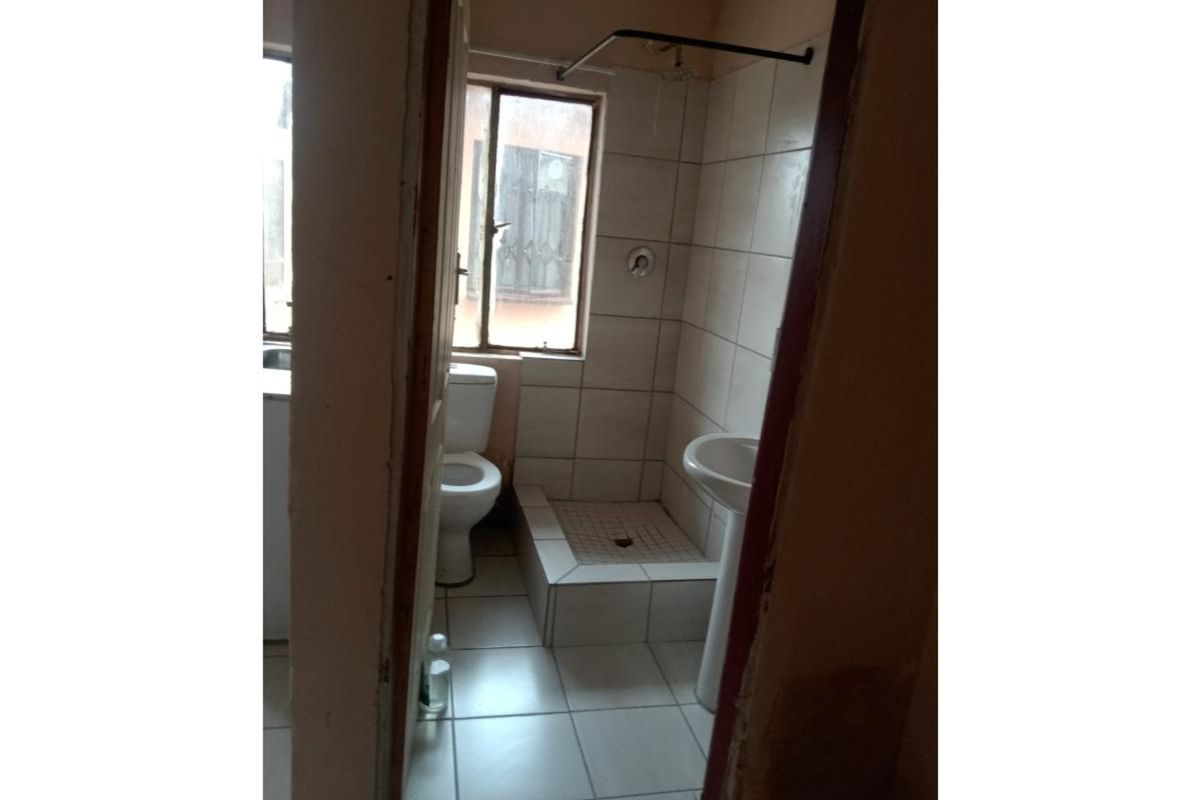 A compact bathroom featuring a raised shower base, pedestal basin, and toilet, requiring cosmetic updates to modernize the space.