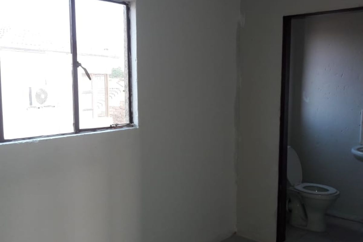 A vacant room with tiled flooring and a window, featuring an adjacent bathroom with a toilet and sink.