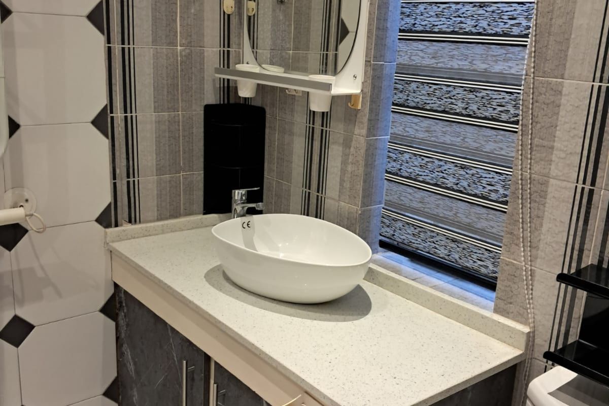 A modern bathroom vanity featuring a stone countertop, vessel sink, chrome faucet, and dark marble-effect cabinetry with integrated storage.