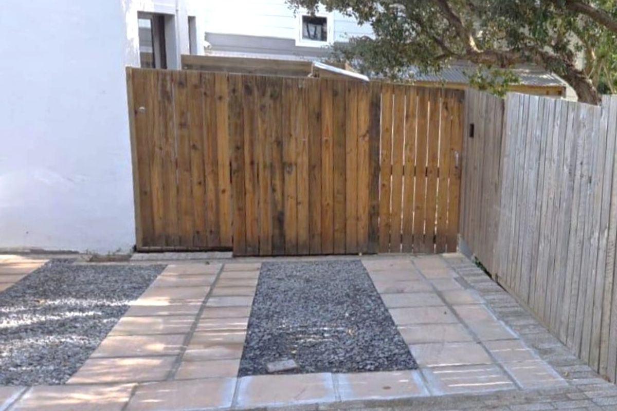 A private outdoor area featuring a combination of paved pathways and gravel sections, enclosed by timber fencing.