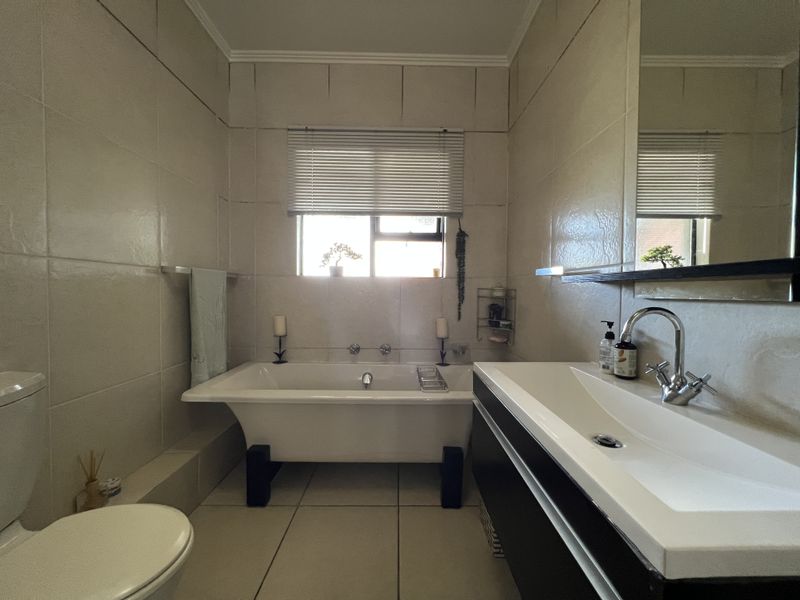 A well-maintained bathroom featuring a modern freestanding bathtub, a sleek wall-mounted vanity with basin, and neutral floor-to-ceiling wall tiles.