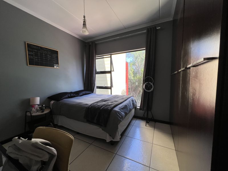 A bedroom featuring tiled flooring, built-in cupboards, and a top-hung window providing natural light.