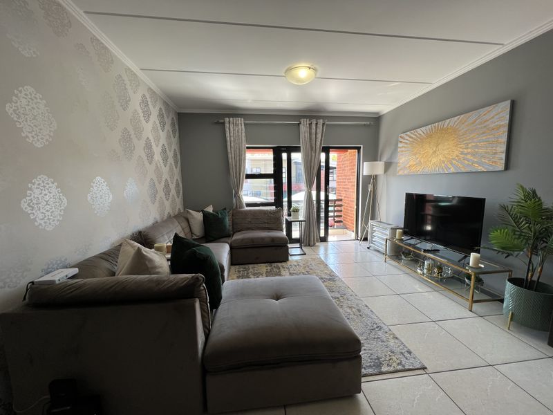 A well-maintained living room featuring tiled flooring, a feature wallpaper wall, and a sliding glass door providing access to an outdoor balcony area.