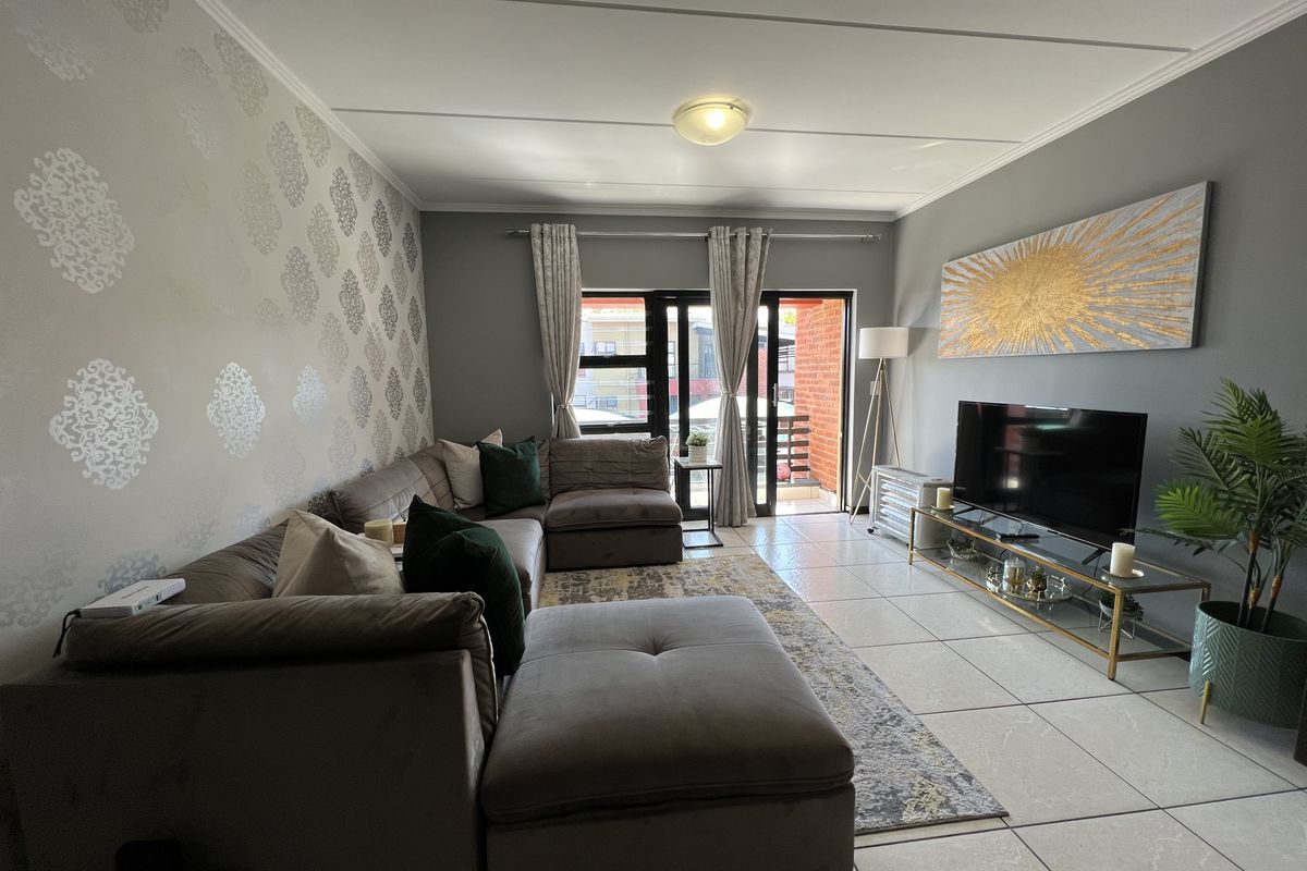 A well-maintained living room featuring tiled flooring, a feature wallpaper wall, and a sliding glass door providing access to an outdoor balcony area.
