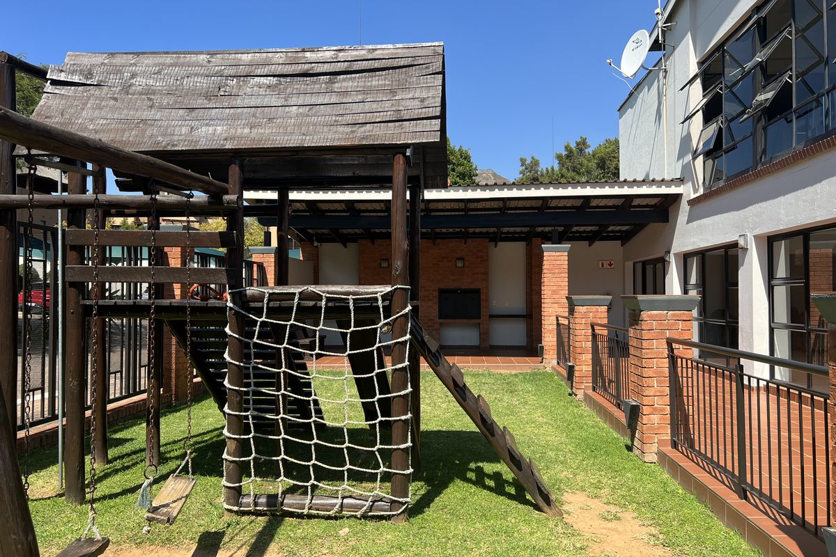 Rear exterior area featuring a covered patio with a built-in braai, brick pillars, and a dedicated children's playground structure on a grass lawn.