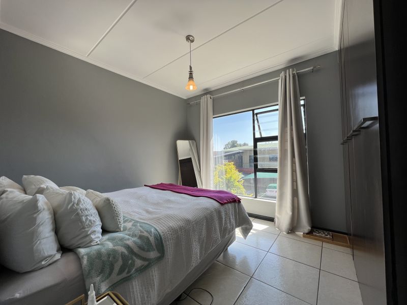 A well-lit bedroom featuring tiled flooring, built-in cupboards, and a large window providing natural light.