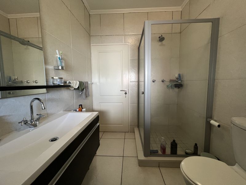 A functional bathroom featuring a glass-enclosed shower, a modern wall-mounted vanity with basin, and neutral floor-to-ceiling wall tiling.