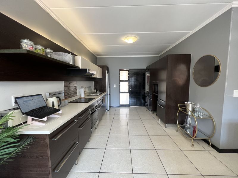 Modern galley-style kitchen featuring dark wood cabinetry, stone countertops, integrated appliances, and tiled flooring, offering a clean and functional workspace.
